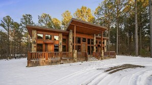 A log cabin with a stone foundation, large windows, and a wooden deck. - Journeys End -2 BR-Timber Creek Trails (Broken Bow)