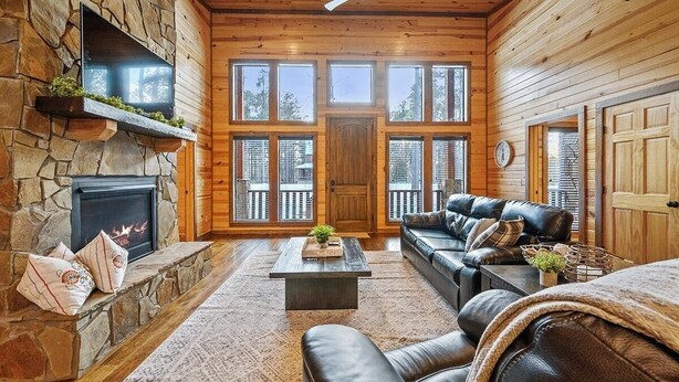 A cozy cabin interior with a stone fireplace, leather sofa, and large windows. - Journeys End -2 BR-Timber Creek Trails (Broken Bow)