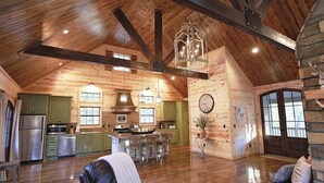 A spacious loft-style interior with a high ceiling, exposed wooden beams, a central island kitchen, and a cozy seating area. - Maison de Crique- Studio -Timber Creek Trails (Broken Bow)