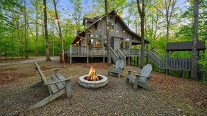A rustic cabin with a deck, a fire pit, and wooden chairs. - Maison de Crique- Studio -Timber Creek Trails (Broken Bow)