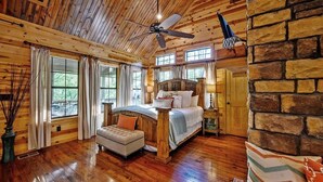 A log cabin bedroom with a wooden ceiling, a bed, a ceiling fan, and large windows. - Maison de Crique- Studio -Timber Creek Trails (Broken Bow)