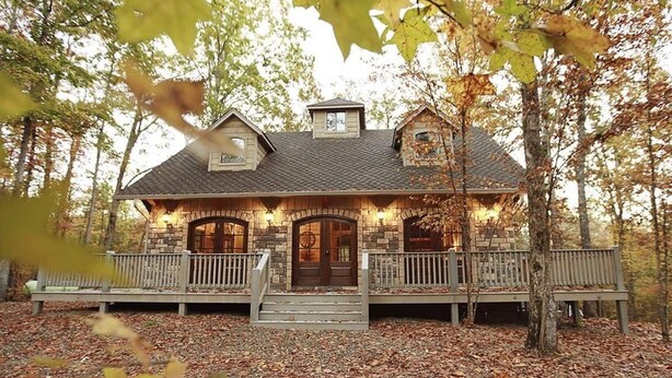 A stone house with a wooden porch, a chimney, and a front door. - Maison de Crique- Studio -Timber Creek Trails (Broken Bow)