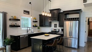 Una cocina moderna con armarios negros, un refrigerador de acero inoxidable y una isla central con taburetes de bar.