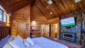 Un dormitorio tipo cabaña con una cama, un televisor fijado a una pared de piedra y una chimenea.