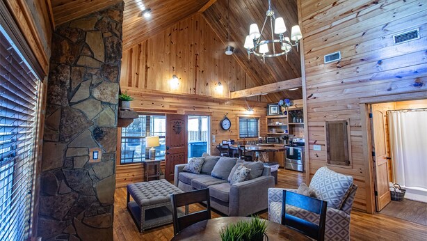 Interior acogedor de una cabaña de madera con detalles en pared de piedra, una zona de comedor con mesa redonda y una cocina con microondas y estufa.