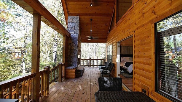 Une terrasse en bois avec des piliers en pierre, un ventilateur de plafond et une vue sur la forêt.