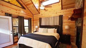 Une chambre à coucher aux murs lambrissés, avec un lit, deux tables de chevet dotées de lampes, une fenêtre encadrée de pierres et une cheminée.