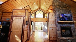 L’intérieur d’une cabane en rondins, avec une cheminée en pierre, des murs en bois et un plafond haut.