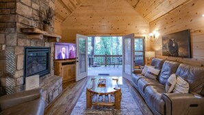 A cozy cabin interior with a stone fireplace, a television, a leather couch, and a wooden coffee table. - Hillside Delight-1 BR-Timber Creek Trails (Broken Bow)