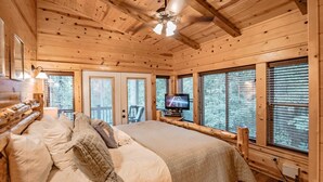 A wooden cabin bedroom with a large bed, a ceiling fan, and a television on a wooden stand. - Hillside Delight-1 BR-Timber Creek Trails (Broken Bow)