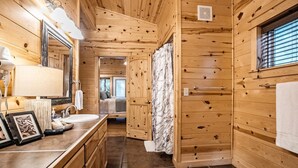 A wooden cabin bathroom with a large mirror, sink, and shower area. - Hillside Delight-1 BR-Timber Creek Trails (Broken Bow)