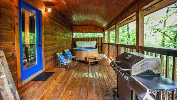 Terraza de madera con jacuzzi, parrilla y mobiliario exterior.