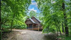 Una cabaña con terraza de madera, rodeada de árboles verdes y frondosos.