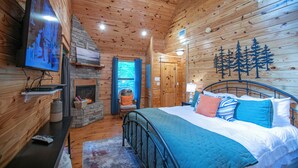 Un dormitorio de cabaña de madera acogedor, con una cama, una chimenea, un televisor y una pared de piedra.