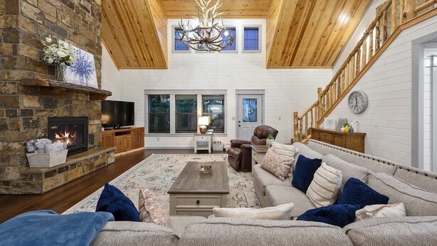 A spacious living room with a stone fireplace, wooden ceiling, and a large sofa with blue cushions.