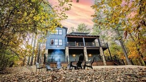 A two-story cabin surrounded by trees with a balcony on the upper floor.