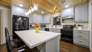 A modern kitchen with white cabinetry, a central island, stainless steel appliances, and a wooden ceiling.