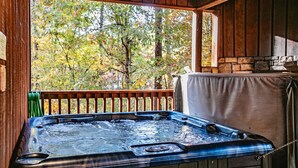 Een hottub in een houten chalet met een stenen openhaard en uitzicht op bomen.
