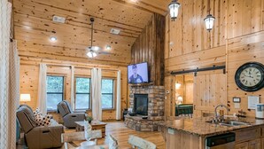 Een gezellig interieur van een chalet met een stenen open haard, houten wanden, een televisie en een keukenhoek.