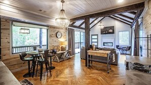 A spacious kitchen with wooden flooring, a dining area with a table and chairs, and a large window providing a view of the outdoors. - Cherokee Rose- 1BR-Northern Hills (Broken Bow)