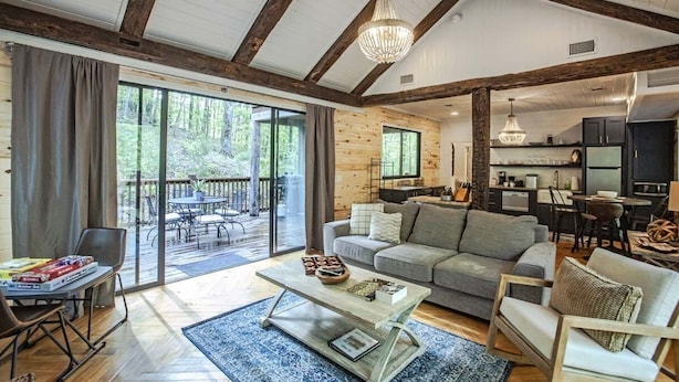 A spacious living area with a wooden ceiling, a large window, and a cozy seating arrangement. - Cherokee Rose- 1BR-Northern Hills (Broken Bow)