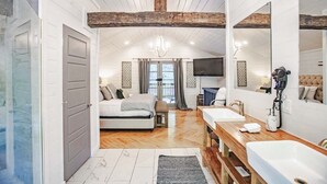 A bedroom with a bed, a TV, and a bathroom with a sink and mirror. - Cherokee Rose- 1BR-Northern Hills (Broken Bow)