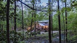 A rustic cabin surrounded by a forest with a stone exterior and a wooden deck. - Cherokee Rose- 1BR-Northern Hills (Broken Bow)