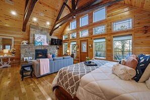 Une chambre aménagée dans un chalet en rondins, avec une cheminée, un canapé, un lit et de grandes fenêtres.