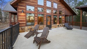 Eine Blockhütte mit Steinuntergrund, großen Fenstern und einer Veranda mit Sitzgelegenheit.