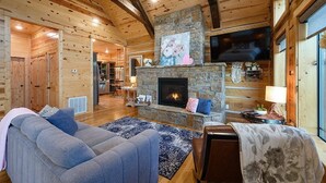 Ein gemütliches Blockhaushaus-Interieur mit Kamin aus Stein, Holzwänden, einer Couch und einem Essbereich.