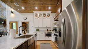 A modern kitchen with white cabinets, stainless steel appliances, and a wooden ceiling. - Ravenswood -2 BR+loft-Eagle Mountain East (Broken Bow)