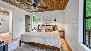 A bedroom with a wooden ceiling, a large bed, a nightstand, and a window with a view of greenery. - Ravenswood -2 BR+loft-Eagle Mountain East (Broken Bow)