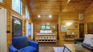 A log cabin interior with a bed, a blue armchair, a wooden table, and a sofa. - Summer Brook Studio-Creekside-Timber Creek Trails (Broken Bow)