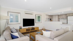 Una sala de estar moderna con un televisor de pantalla plana, dos sofás, una mesa de centro y una cocina al fondo.