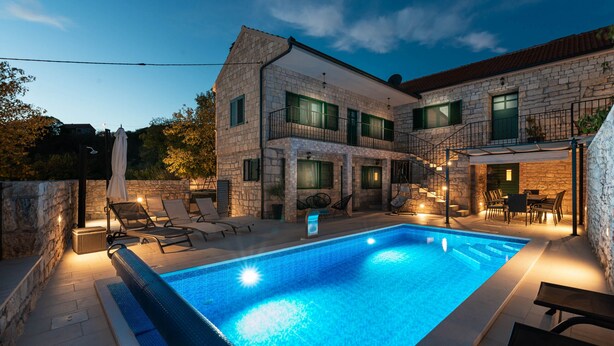 Un edificio de piedra con piscina, mobiliario exterior y una escalera que conduce a un segundo piso.