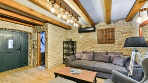 Una sala de estar acogedora con pared de piedra, vigas de madera, un sofá gris, una mesa de centro de madera y una lámpara.
