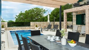Zona de piscina con mesa lista para comer, sillas de descanso y pared de piedra.