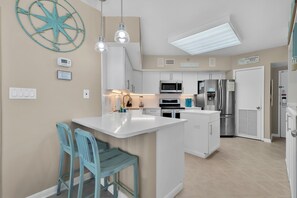 Une cuisine moderne avec des meubles blancs, un îlot central et des tabourets de bar bleus.