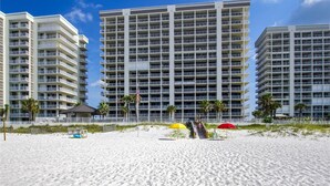 Un hôtel en bord de mer, avec plusieurs étages, des balcons et une plage de sable au premier plan.