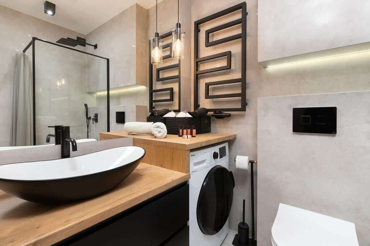 Un baño moderno con un lavamanos de diseño, lavadora, inodoro y cabina de ducha de vidrio.