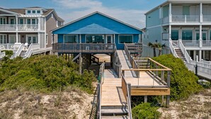 Une propriété située en bord de mer, avec une maison bleue, des allées en bois et une clôture blanche.