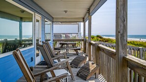 Une terrasse en bois avec des chaises longues et une table, donnant sur une plage.