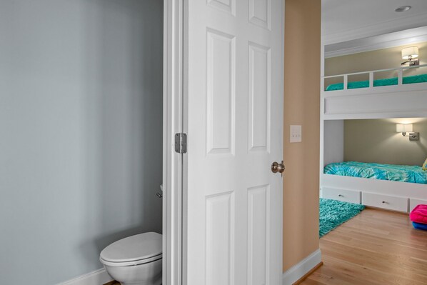 A room with a white door, a toilet, a bunk bed with teal bedding, and a small rug.