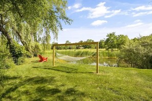 A hammock set up on a wooden frame in a grassy area with a pond and trees in the background. - The Greenhouse: Modern Rural Escape with Fire Pit (Ithaca)