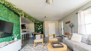 A modern living room with a green wall, a flat-screen TV, a sofa, two armchairs, and a coffee table. - The Greenhouse: Modern Rural Escape with Fire Pit (Ithaca)