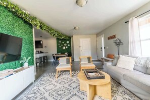 A modern living room with a green wall, a flat-screen TV, a sofa, two armchairs, and a coffee table. - The Greenhouse: Modern Rural Escape with Fire Pit (Ithaca)