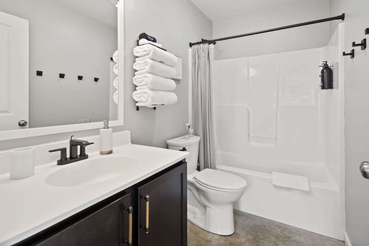 A modern bathroom with a white sink, dark cabinets, a toilet, and a shower area.