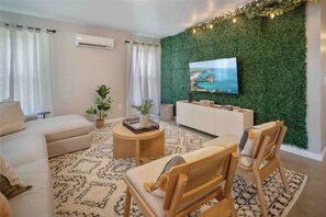 A living room with a green wall, a TV, a sofa, a coffee table, and a chair. - The Greenhouse: Modern Rural Escape with Fire Pit (Ithaca)