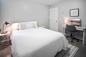 Une chambre d’hôtel avec un lit, un bureau, une chaise, une lampe, une télévision et un tableau encadré au mur.