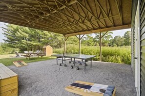 An outdoor covered patio with a ping pong table, picnic table, and lounge chairs. - The Greenhouse: Modern Rural Escape with Fire Pit (Ithaca)